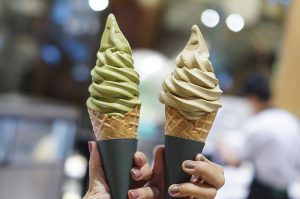 Woman holding two soft ice cream, matcha and hojicha at Japanese dessert cafe.